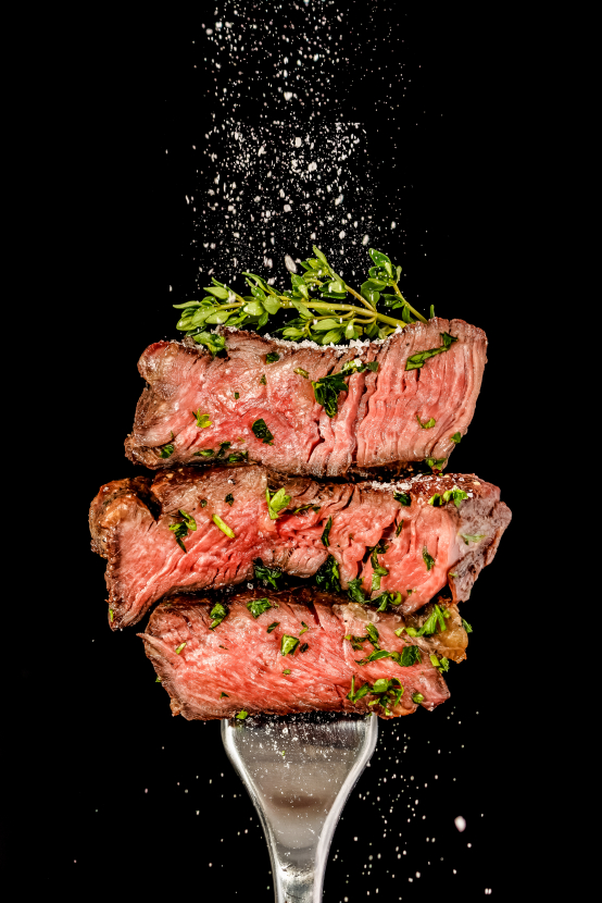 Aufgeschnittenes Rindersteak, saftig und medium gebraten. Aufgespießt auf einer Gabel, mit Kräuter und Salz.