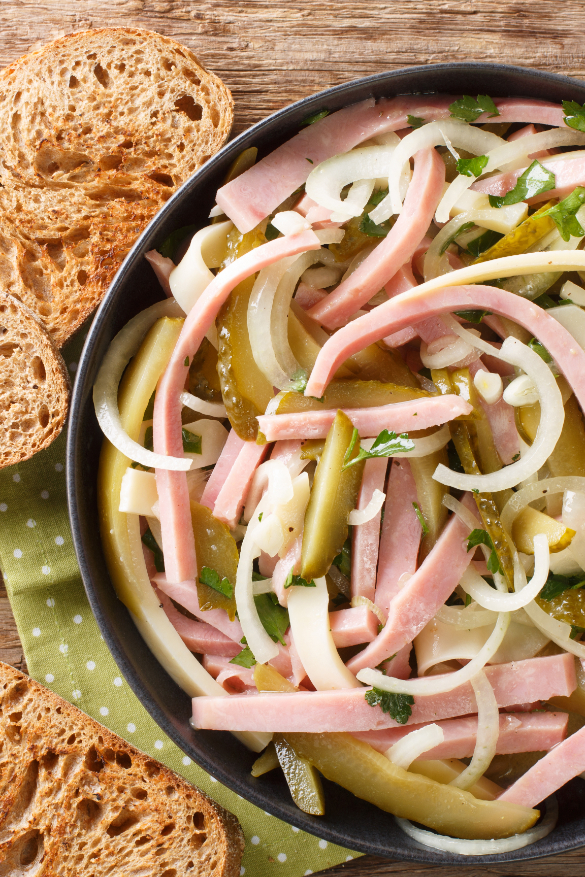 Wurstsalat mit Käse, Zwiebeln und Essiggurken, serviert mit Brot – frisch angerichtet.